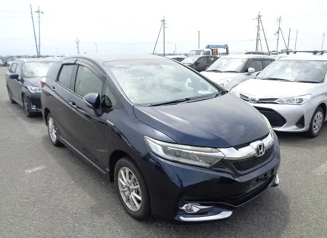 A Blue Honda Car, Potentially Part Of A Car Sale, Is Parked In A Lot With Other Vehicles. The Front And Side Are Visible Under An Overcast Sky, With Utility Poles In The Background.